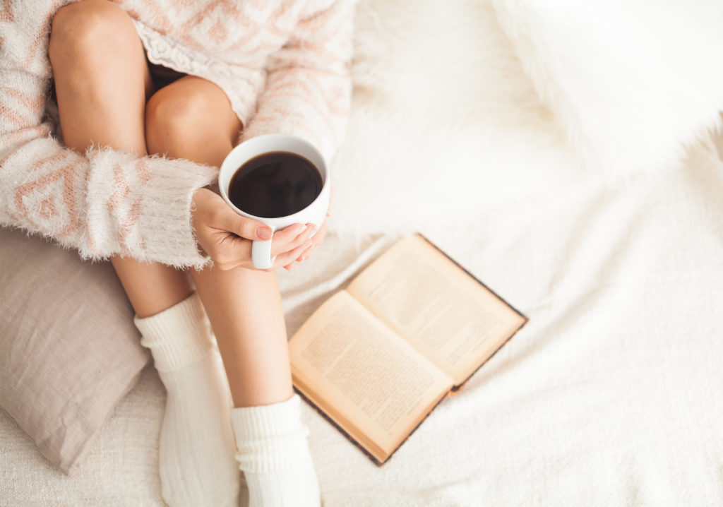 Soft photo of woman on the bed with old book and cup of coffee in hands, top view point